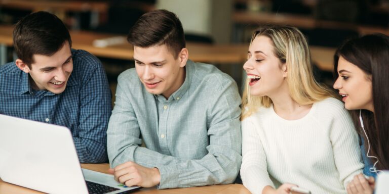 A group of four people in front of a computer laughing and talking